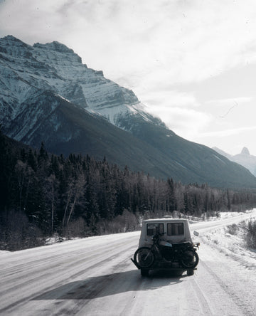 Peter Lik driving his vintage white van with motorcycle on rear bumper driving through the snow covered roads in Alaska.