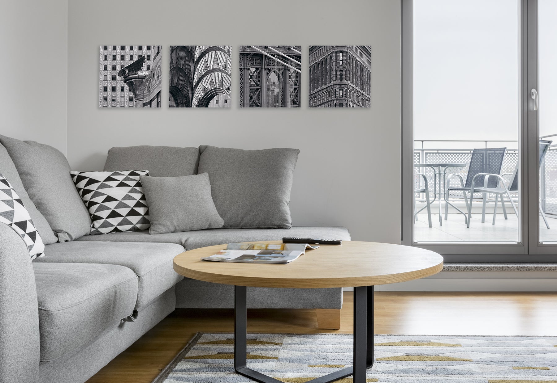 Living room with light gray couch and light brown coffee table featuring four square black and white photographs of iconic New York City landmarks by Peter Lik