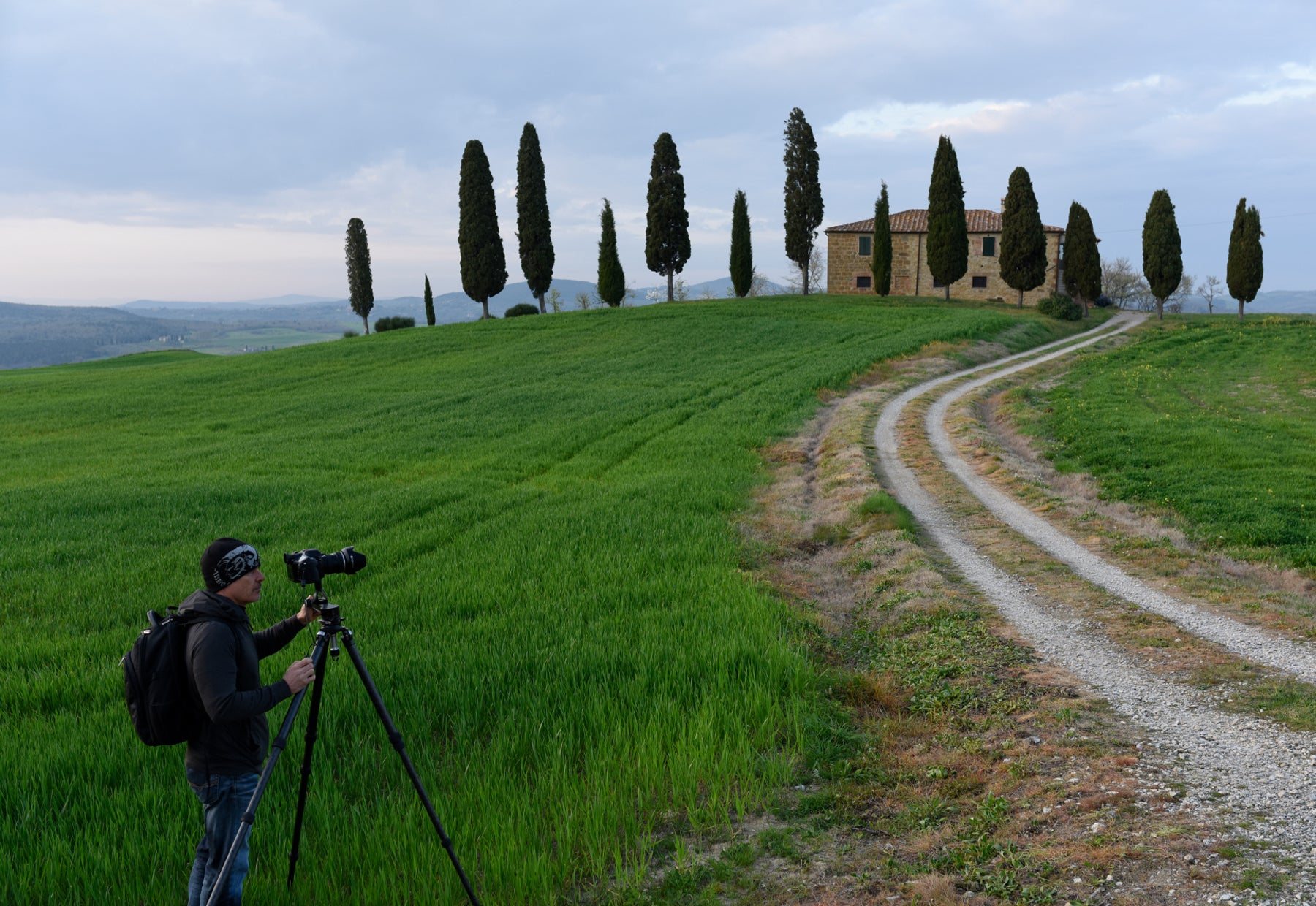 Portrait of Peter Lik with his tripod at the grassy entrance of a tree-lined chalet in Tuscany, Italy
