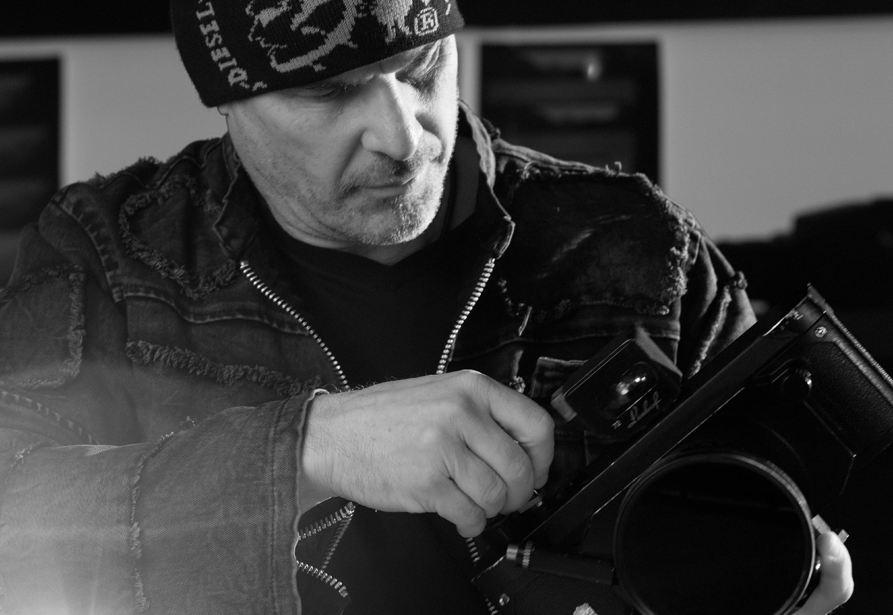Black and white portrait of Peter Lik wearing a black leather jacket and beanie advancing film in his Linhoff 617 III camera