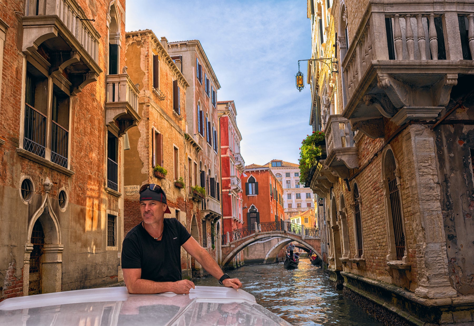 Portrait of Peter Lik in a baseball cap standing in a boat traveling through the canals of Venice, Italy.