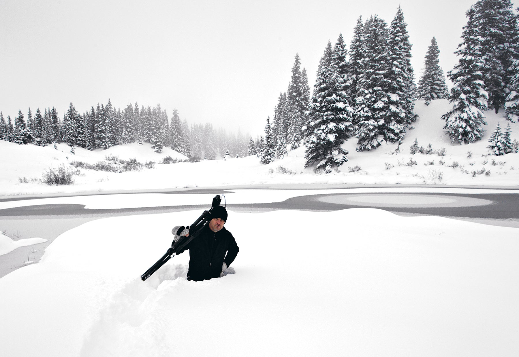 Portrait of Peter Lik with a tripod over his shoulder standing waist deep in the winter snow at Yosemite National Park