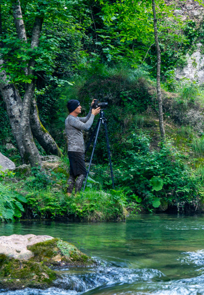 Portrait of Peter Lik wearing a gray shirt and beanie taking a photograph on the waters edge in Casaletto Spartano, Italy