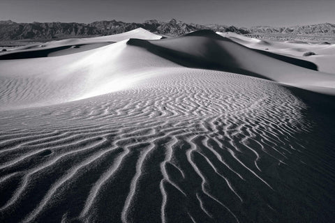 Black and white windswept sand dunes of Death Valley California with rock hills in the distance