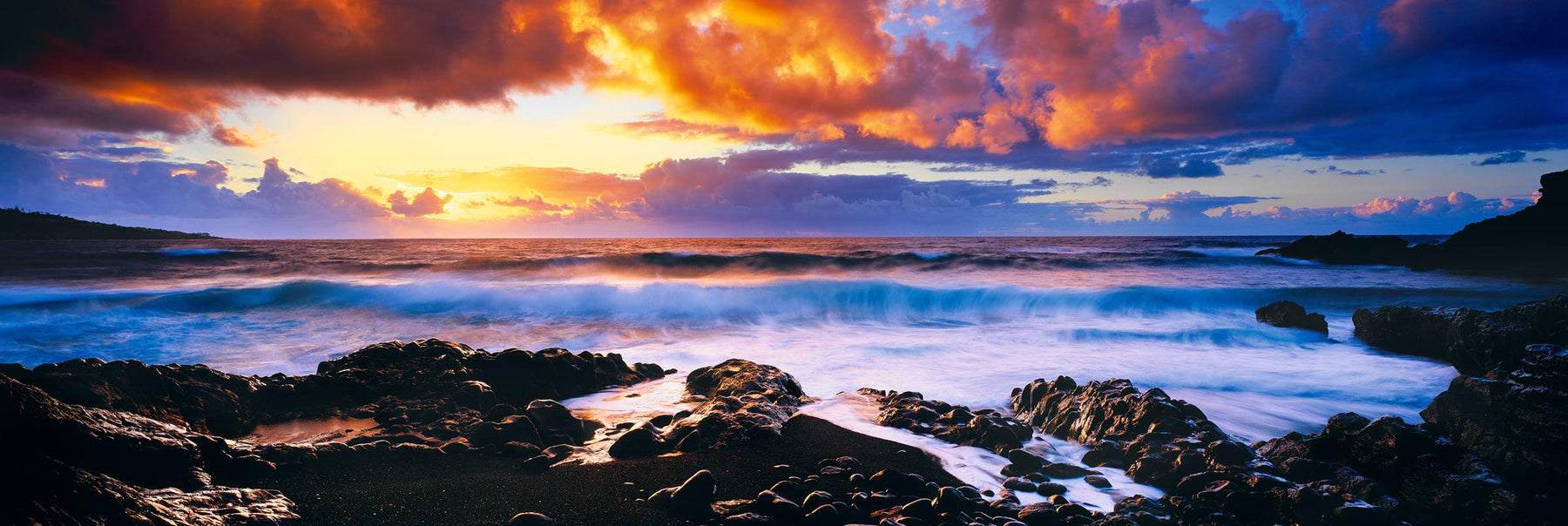 Waves crashing onto a rocky beach in Hana Hawaii with the sun rising into a cloud filled sky