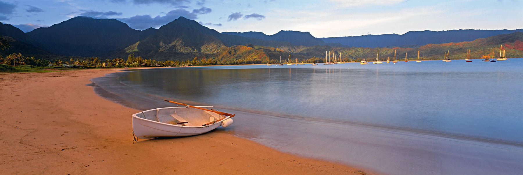 White row boat sitting on the shore of the sail boat filled Hanalei Bay Hawaii with mountains in the background