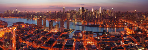 View of New York City from a rooftop lit up at night with the streets glowing orange and red