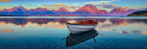 White wooden row boat on Jackson Lake with the sun shining on the mountains