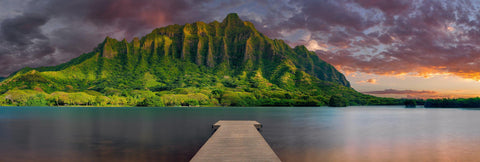 Wood jetty stretching over a lagoon with the sun setting behind the tropical mountain cliffs of Oahu Hawaii