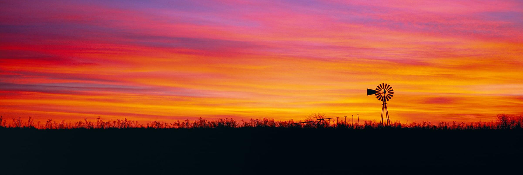 Silhouette of a single windmill and brush field during a colorful sunset in Elk City Oklahoma
