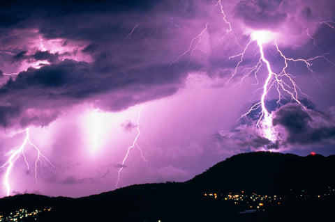 Lightning in the cloudy purple sky over the hills of the Copperlode Dam in Australia at night