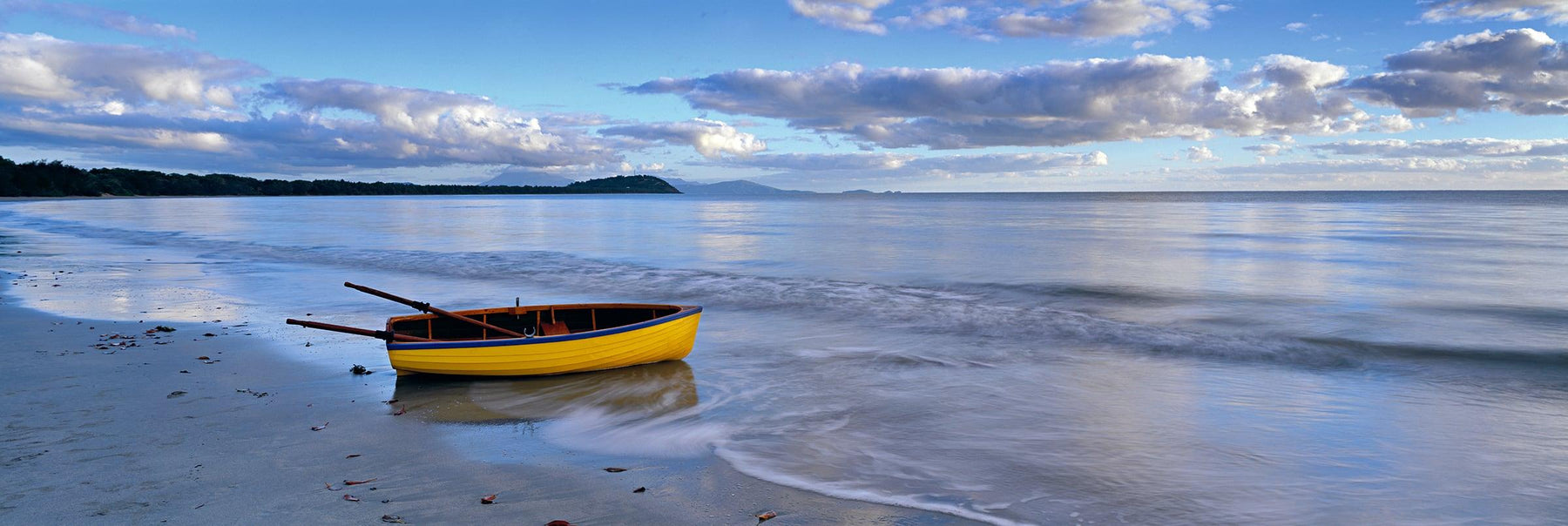 Yellow rowboat washed a shore on the wet sand beach in Port Douglas Australia