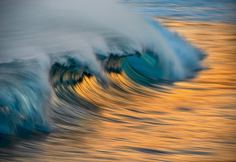 Close up of a turquoise wave reflecting orange from the sun during a sunset 