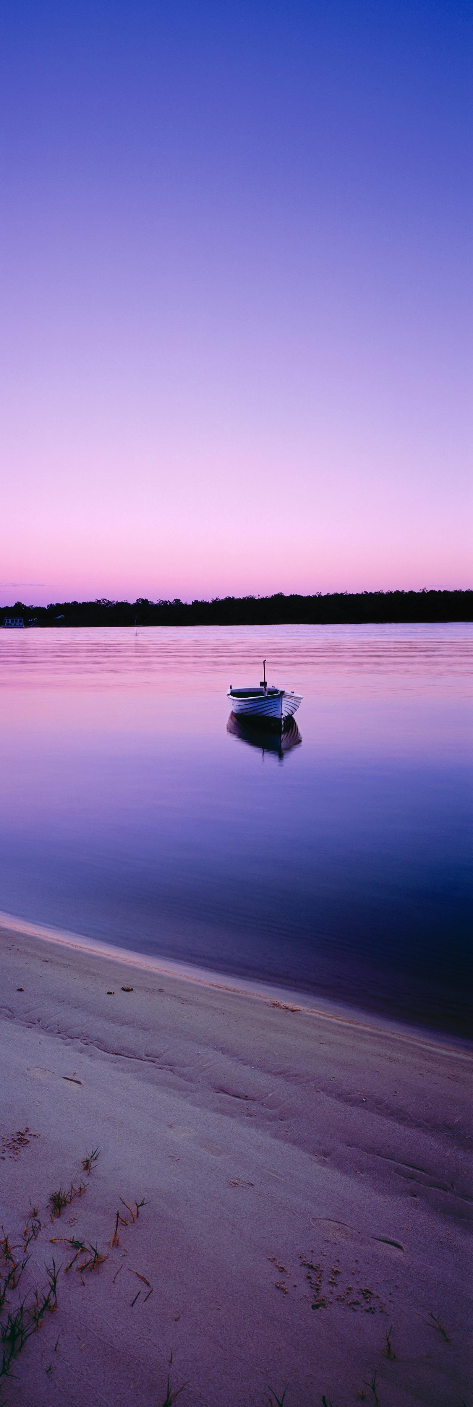 Dinghy floating off the banks of the Noosa River at sunrise with the purple sky reflecting off the water