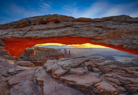 Sun hitting a rock arch that overlooks the buttes and mountains of Canyonlands