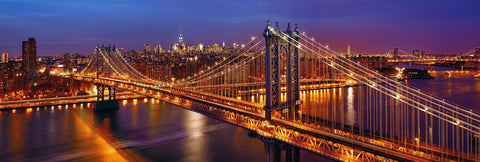 Manhattan Bridge lit up at night overlooking the glow of New York City in the distance