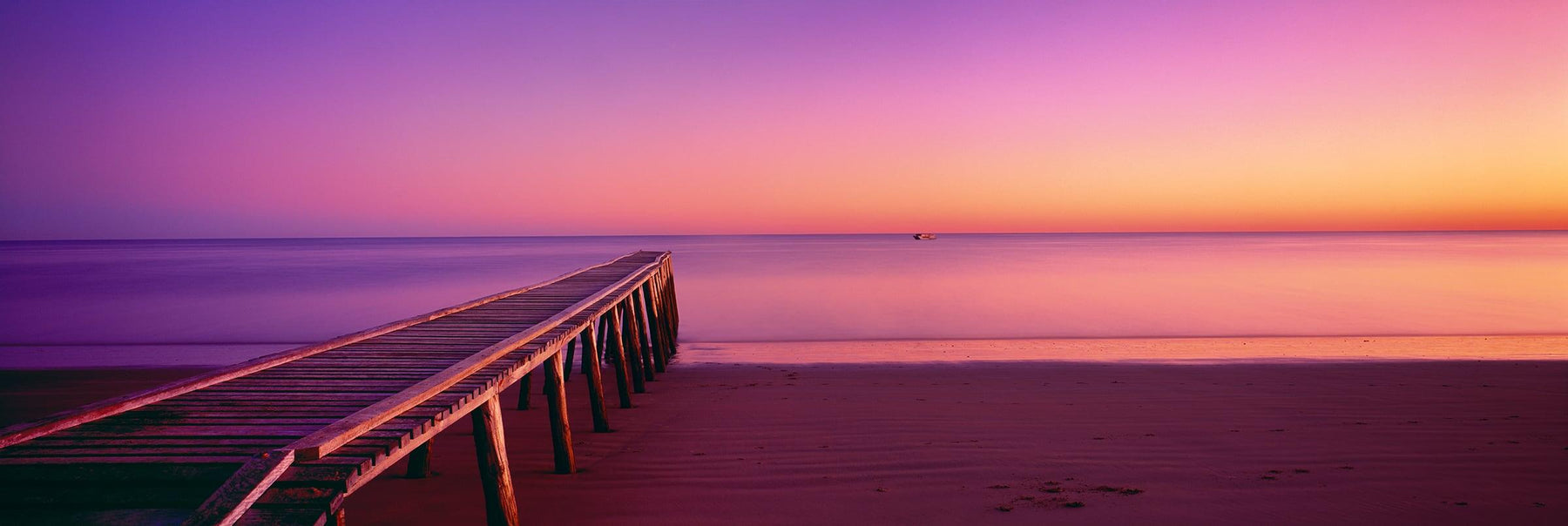 Old timber jetty stretching out over the sand beach of Hervey Bay Australia during a pink sunrise