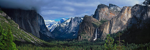 Yosemite Valley covered by clouds with the waterfall and snow covered mountains in the background