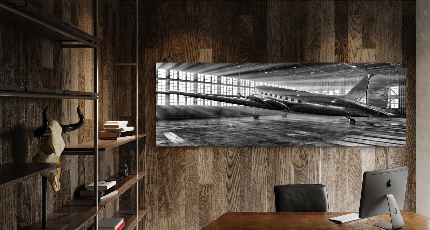 Large black and white image of a vintage silver airplane in a hangar photographed by Peter Lik hanging on the wall of an urban loft 