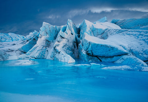 Peter Lik’s Arctic Jewel, featuring sculpted blue ice formations rising above vivid turquoise glacial water beneath a dramatic sky.