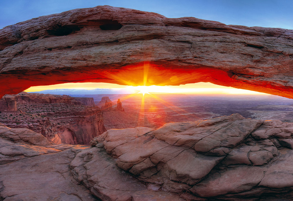 Rock arch in Canyonlands National Park, Utah with a sunburst shining through at sunrise.