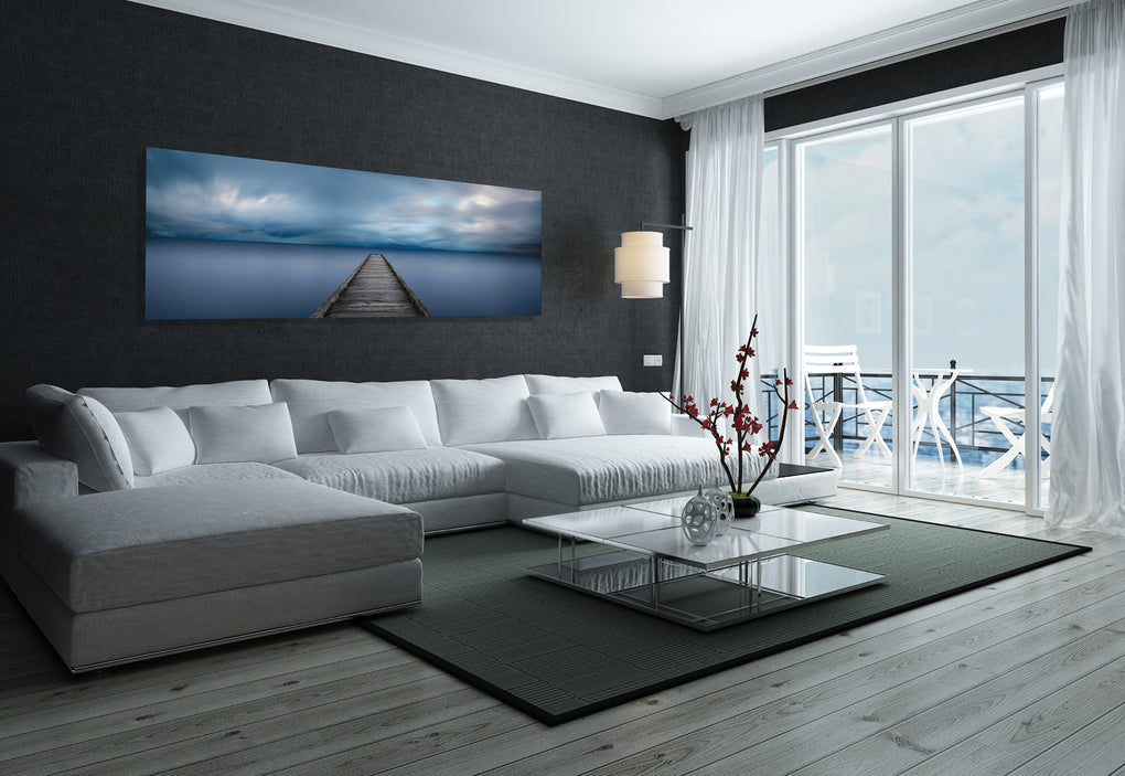 Living room with dark gray wall and white couch featuring a photograph of a pier reaching out into cloudy skies and blue water