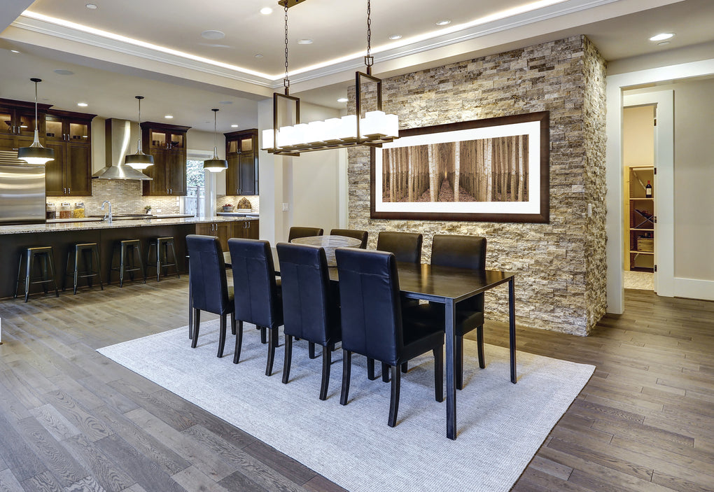 Dining room with wood floors and a stone light brown stone wall featuring a framed photograph of rows of trees