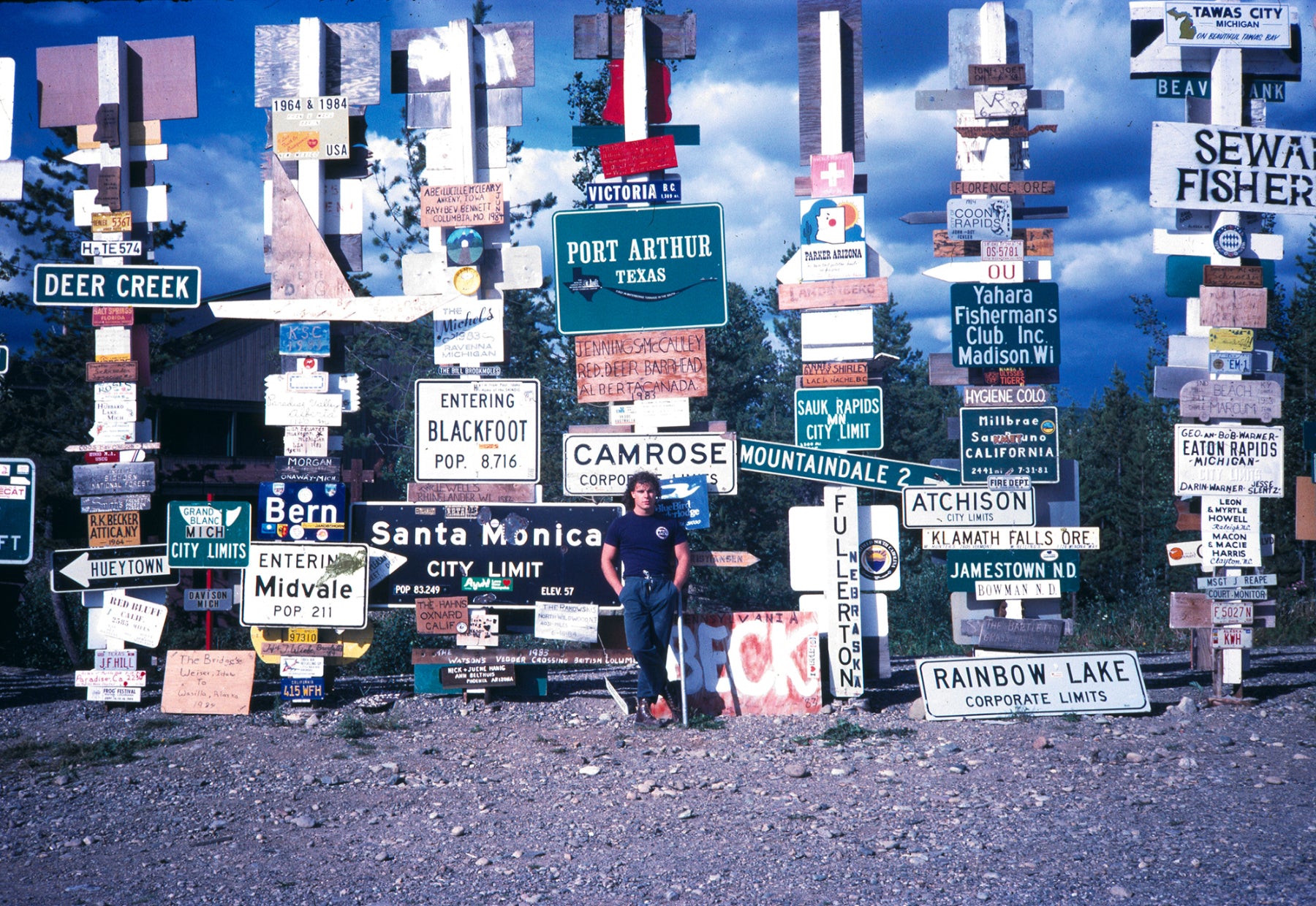 Early portrait of Peter Lik standing in front fo Signpost Forest, Watson Lake along Alaska Highway
