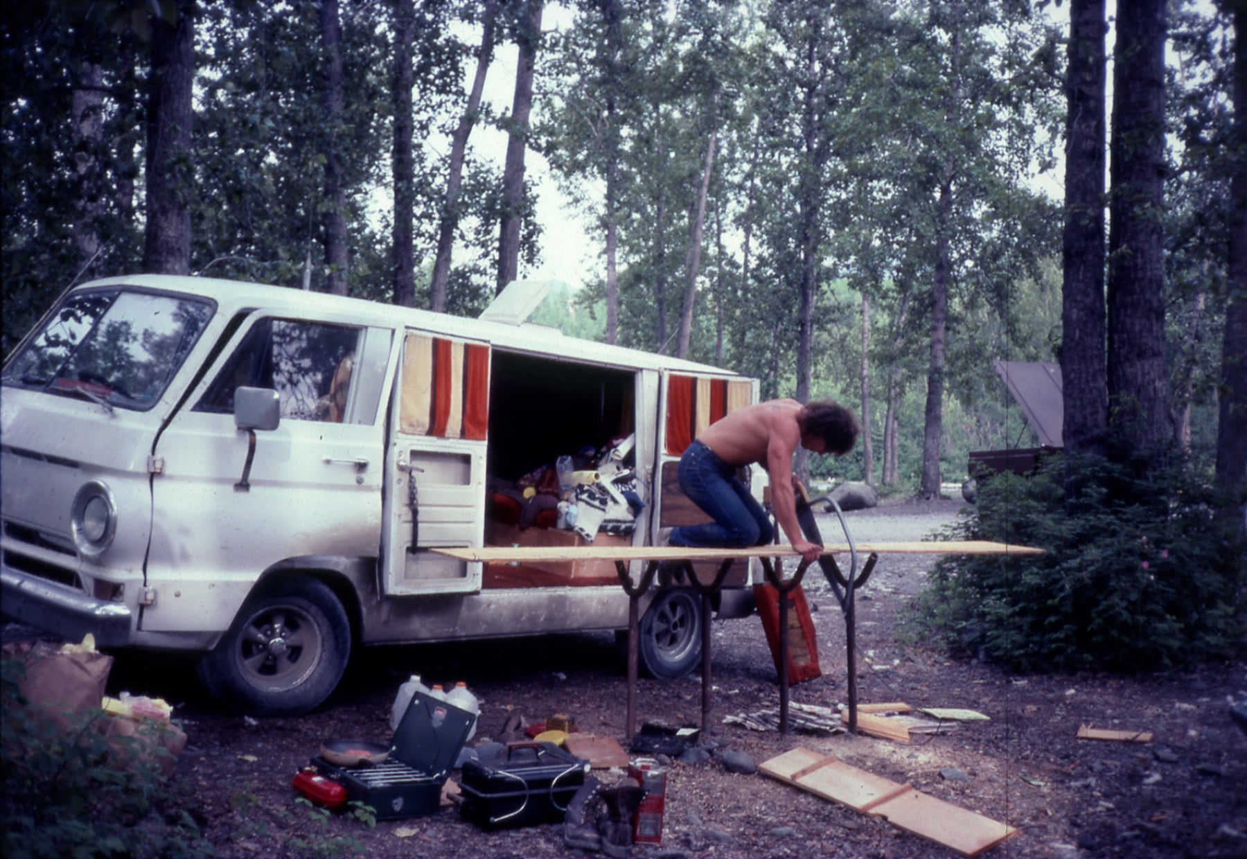 Early photograph of Peter Lik cutting wood next to his vintage white van in the woods of Alaska