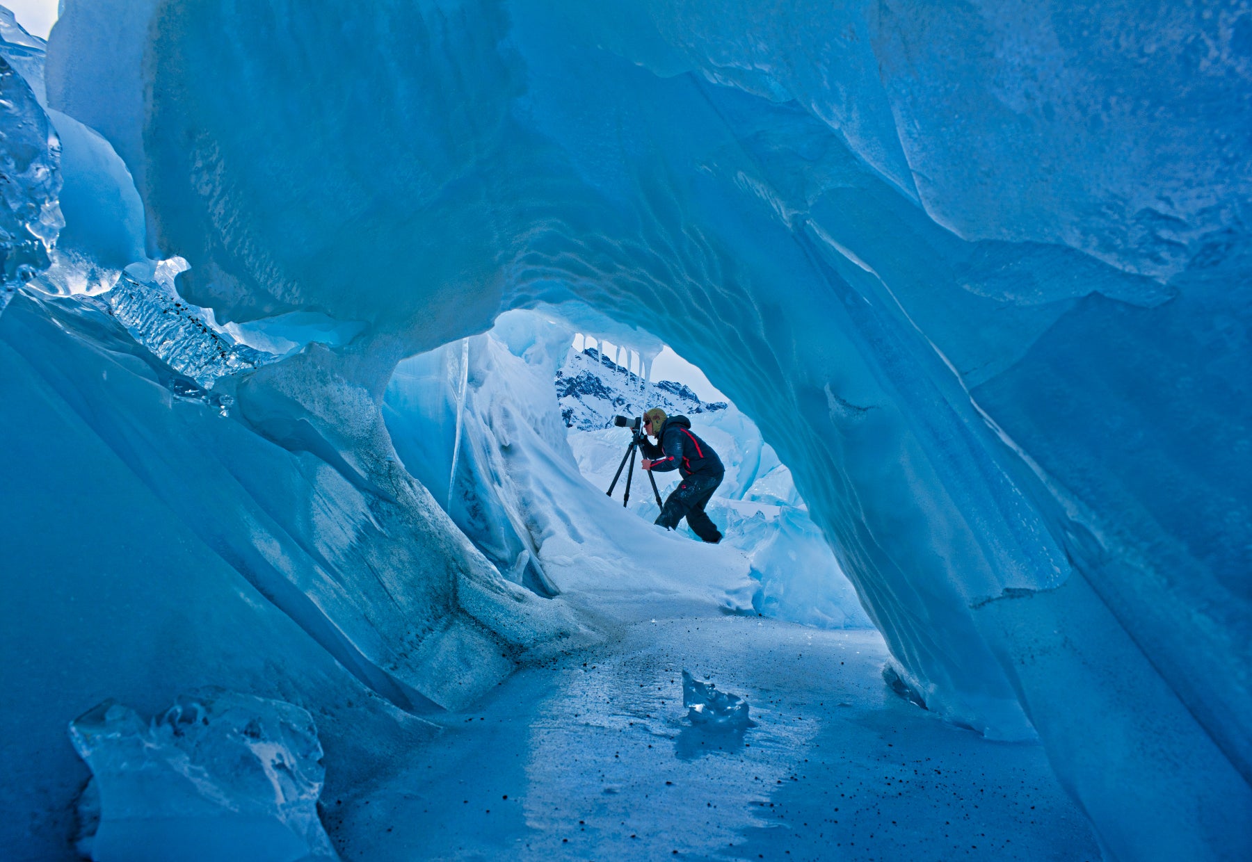 Portrait of Peter Lik looking through a camera from the view through a tunnel of bright blue ice in Alaska.