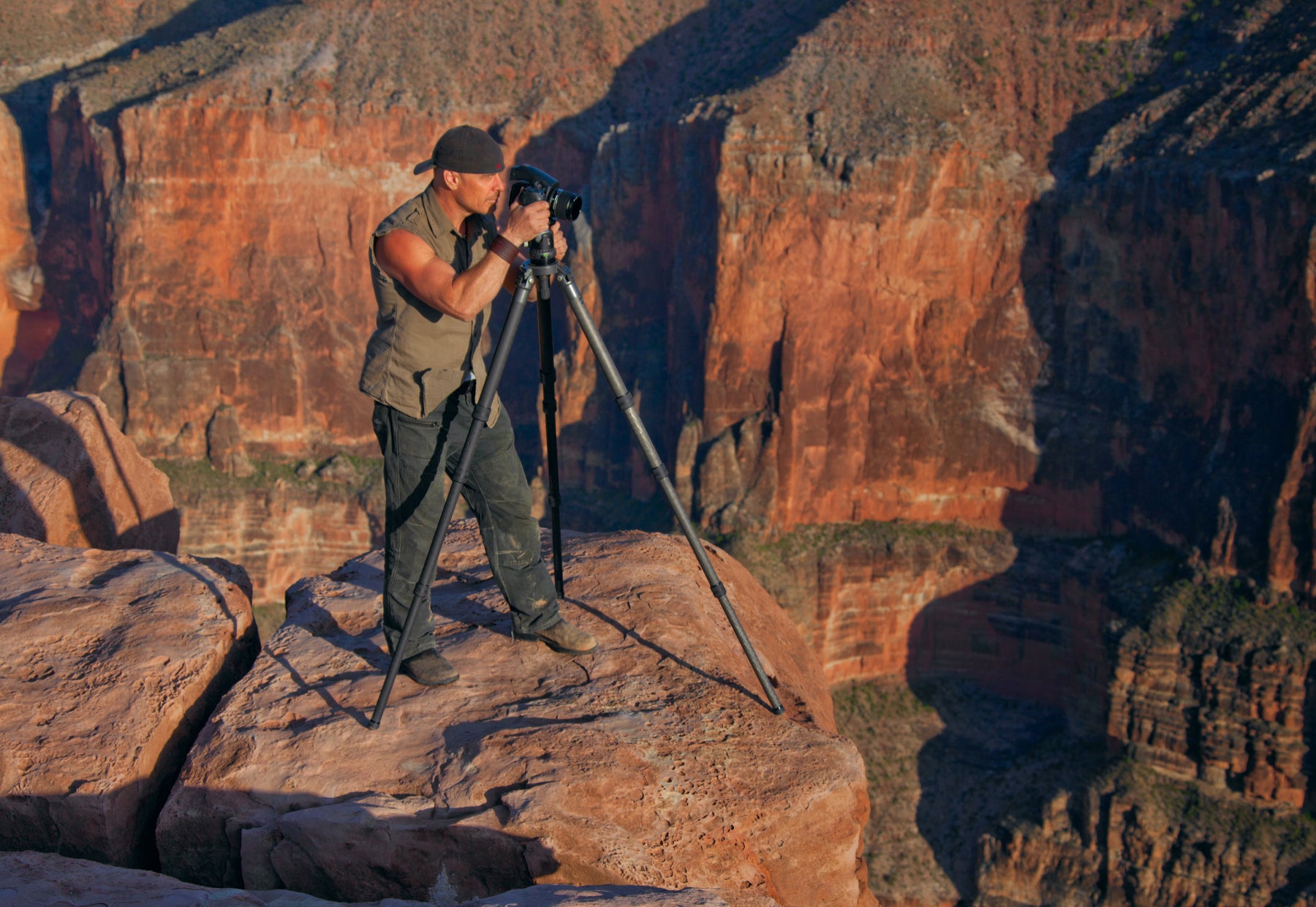 Portrait of Peter Lik in a baseball cap and a shirt with no sleeves taking a picture at the Grand Canyon National Park in Arizona.