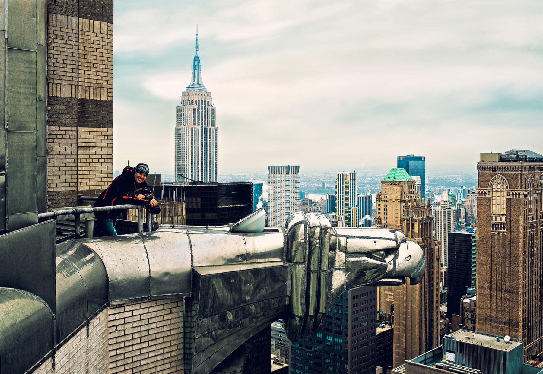 Portrait of Peter Lik captured next to one of the stainless steel Eagle-headed gargoyles on the top of the Chrysler Building with the skyscrapers of New York City in the background