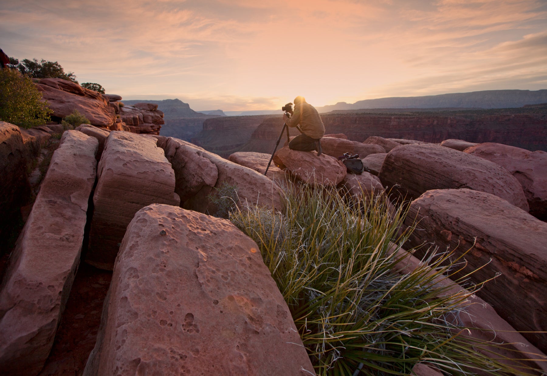 Portrait of Peter Lik kneeling down a rocky wall of Toroweap Overlook at The Grand Canyon National Park in Arizona at sunrise.