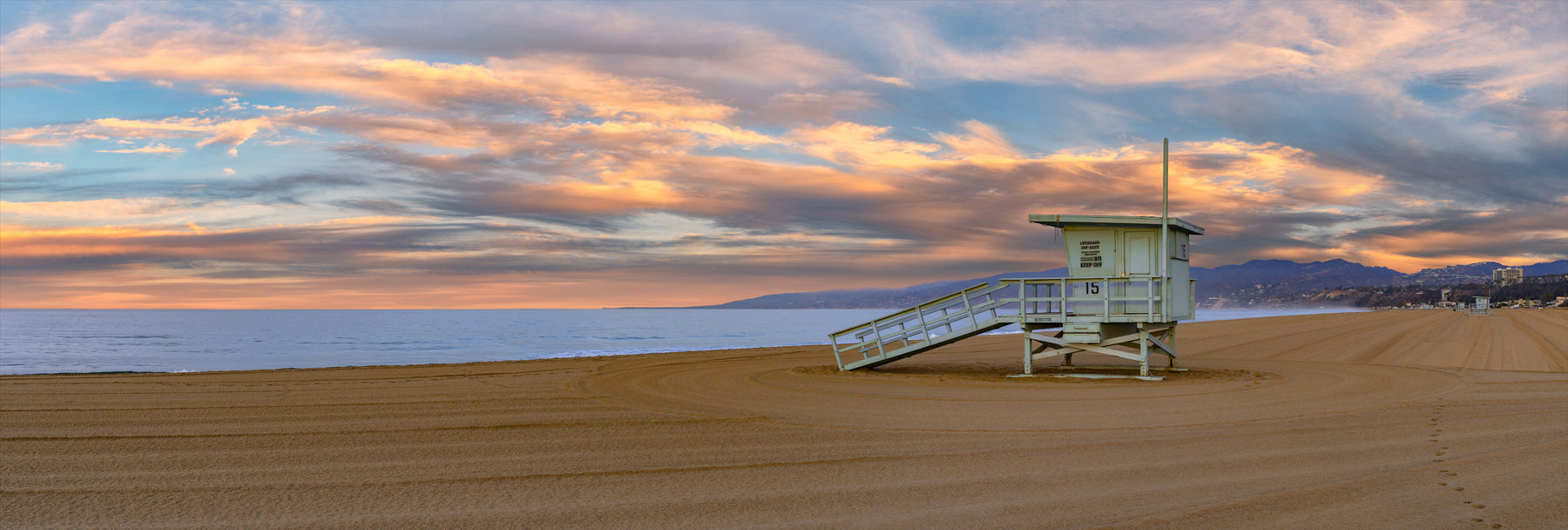 Witness the tranquil beauty of Santa Monica at sunrise, where a solitary lifeguard shack stands against a canvas of pastel skies.