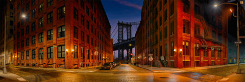 City street at night with illuminated buildings and a bridge in the background