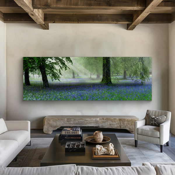 A Peter Lik limited edition photograph of a woodland in England with the sunlight shining onto the purple and white flowers below hanging on the wall of a rustic, refined living room. 