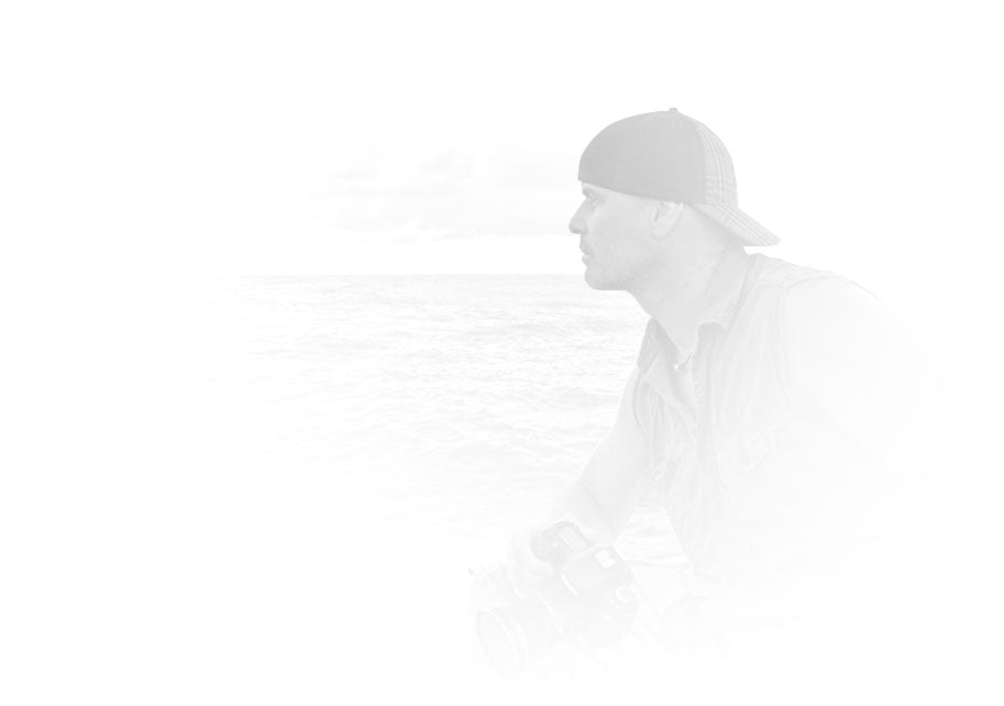 Black and white portrait of Peter Lik in a sleeveless shirt and baseball cap sitting on back of boat looking out at Pacific Ocean