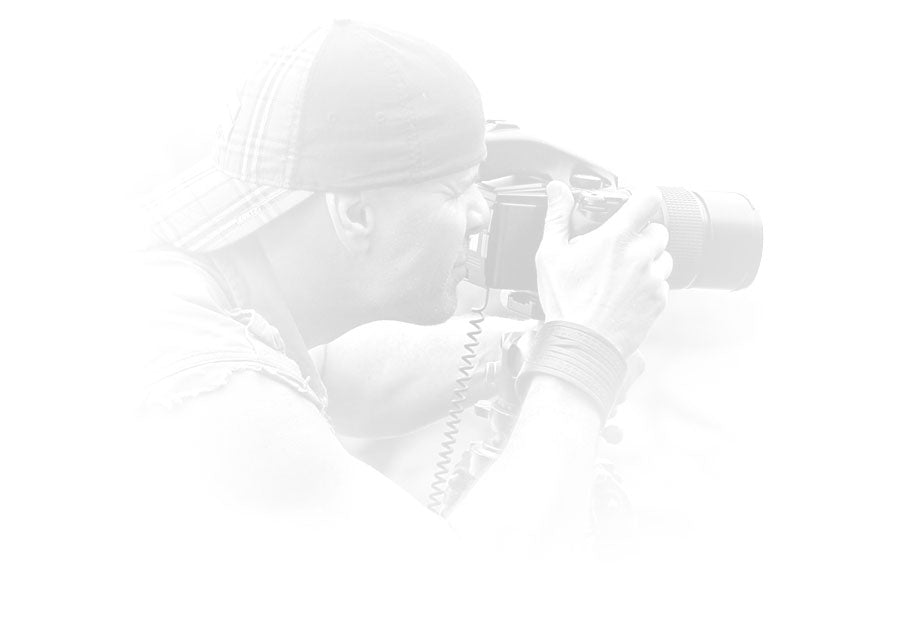 Portrait of Peter Lik wearing a sleeveless shirt and baseball cap taking a photograph with a Phase One camera