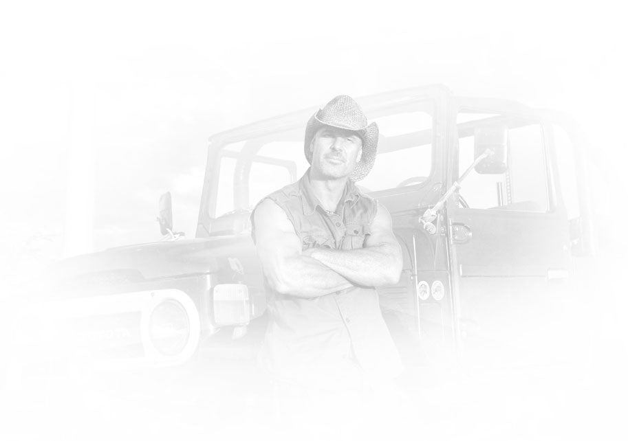 Black and white portrait of Peter Lik wearing a sleeveless shirt and cowboy hat leaning on a Jeep Wrangler