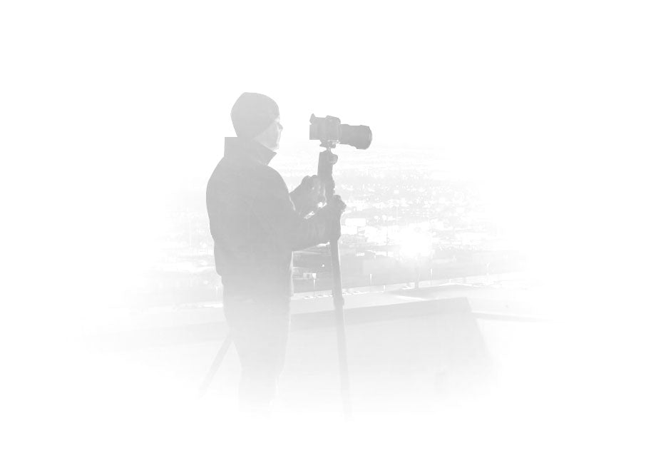 Silhouetted portrait of Peter Lik wearing a jacket and beanie taking a photograph with a camera on a tripod
