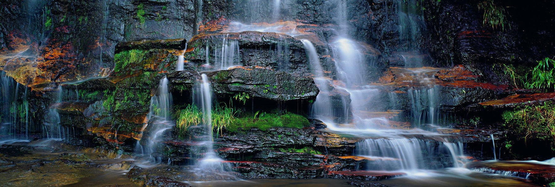 Waterfall pouring over moss covered black rock wall into a pond in the Blue Mountains National Park Australia