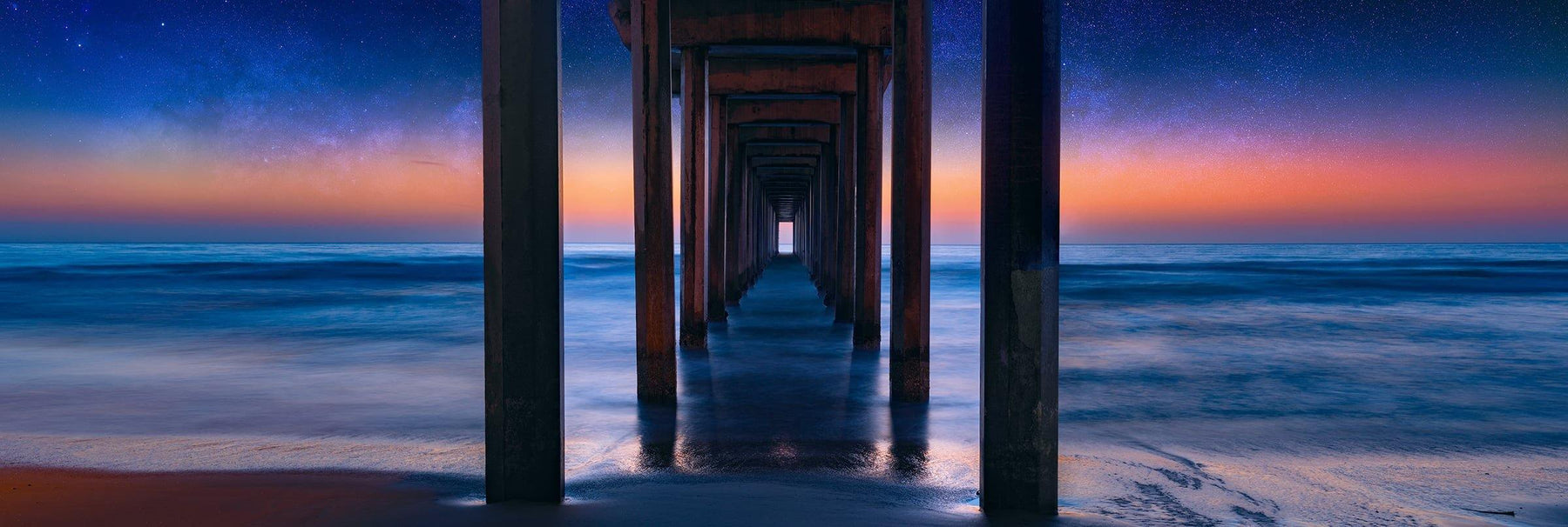 The ocean and Scripps Pier of La Jolla California with the glowing horizon and star filled sky in the background