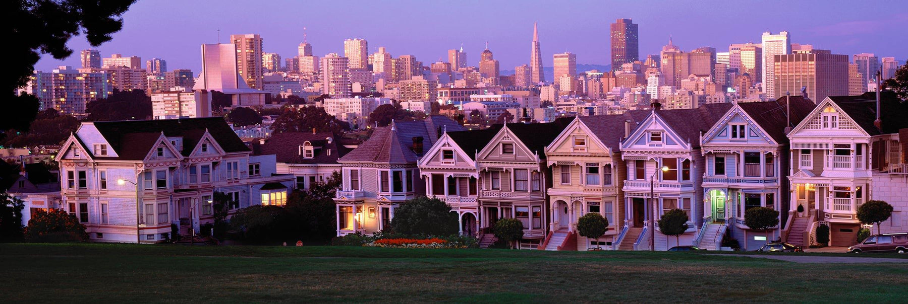 Row of Victorian houses across from a grass area with the skyscrapers of San Francisco in the background