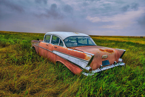 Old rusty red and white car in a grass field in North Dakota during a storm