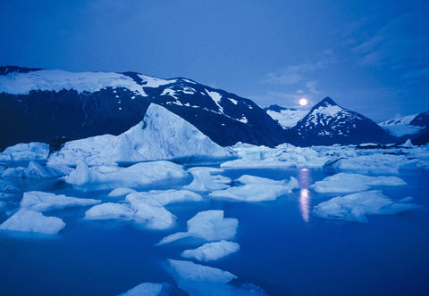 Moon in the sky over the mountains shining onto Portage Glacier and the ice chunks floating in Portage Lake Alaska