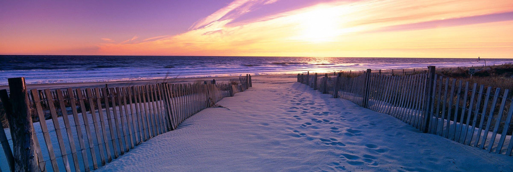Sand pathway with picket fences leading to a beach in Newport Rhode Island during sunrise