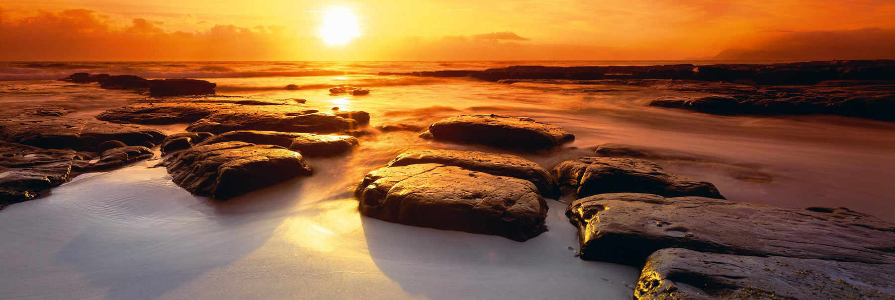 Rocks on a sandy beach during low tide at Wineglass Bay Australia with the sun rising in background