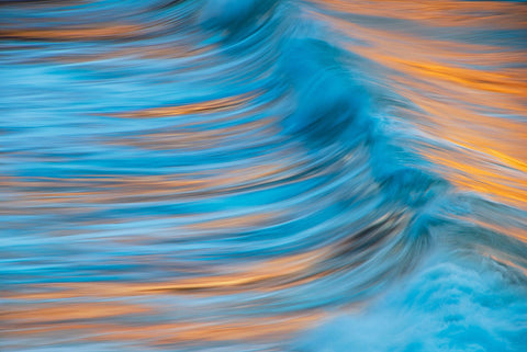Close up of a turquoise wave reflecting orange from the sun during a sunset in Maui Hawaii