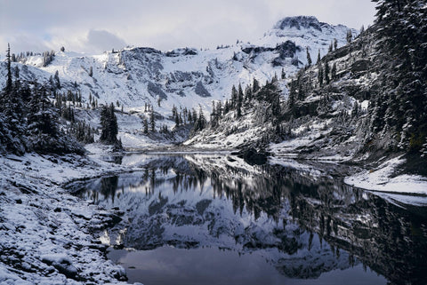 Snow covered shoreline and forest surrounding the a lake in front of Mount Baker Washington