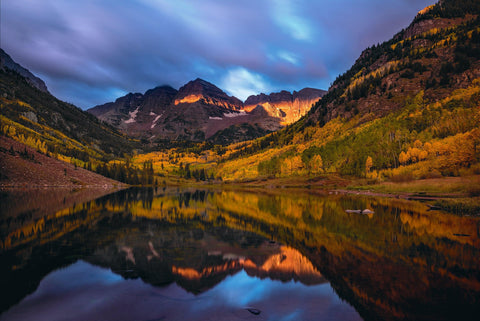 Autumn colored Maroon Bells mountainside and storm clouds overhead reflecting off of Maroon Lake Colorado